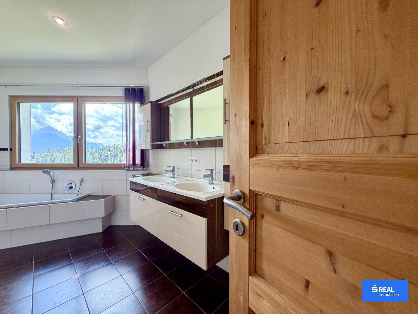 Geräumiges Badezimmer mit Doppelwaschbecken, Badewanne und Bergblick aus dem Fenster.