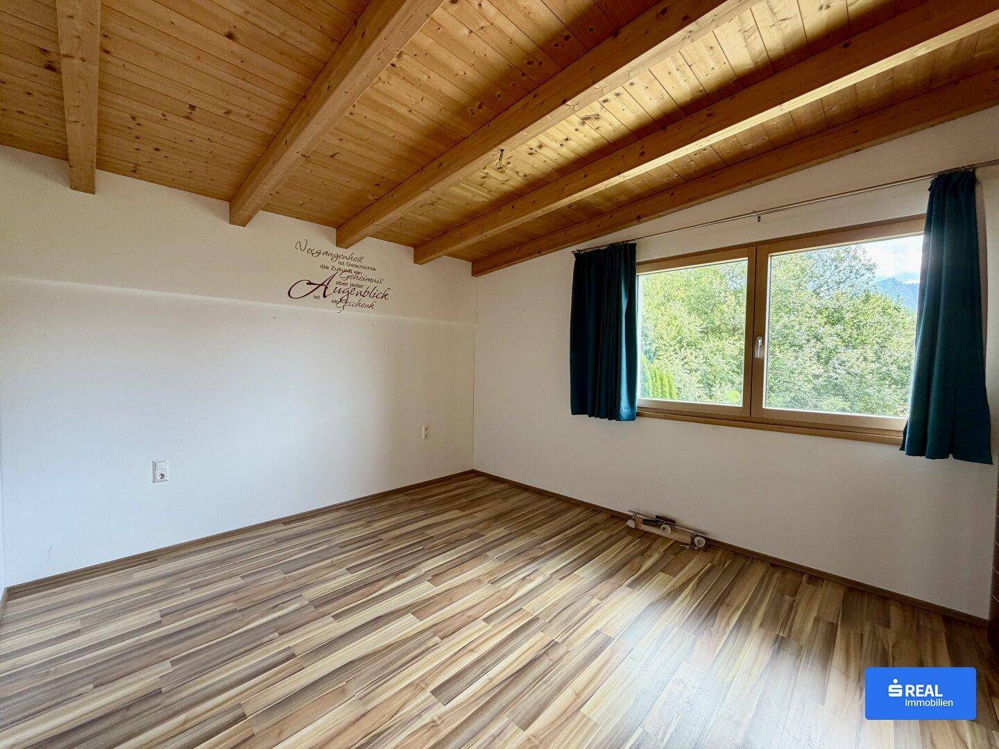 Helles Schlafzimmer mit Holzbalkendecke, Laminatboden und weitem Blick ins Grüne.