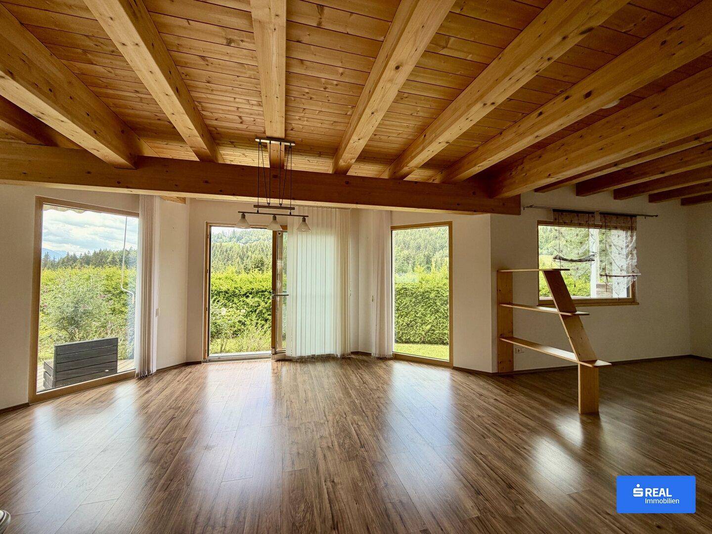 Geräumiges Wohnzimmer mit Holzbalkendecke, Laminatboden und großen Fenstern zum Garten.