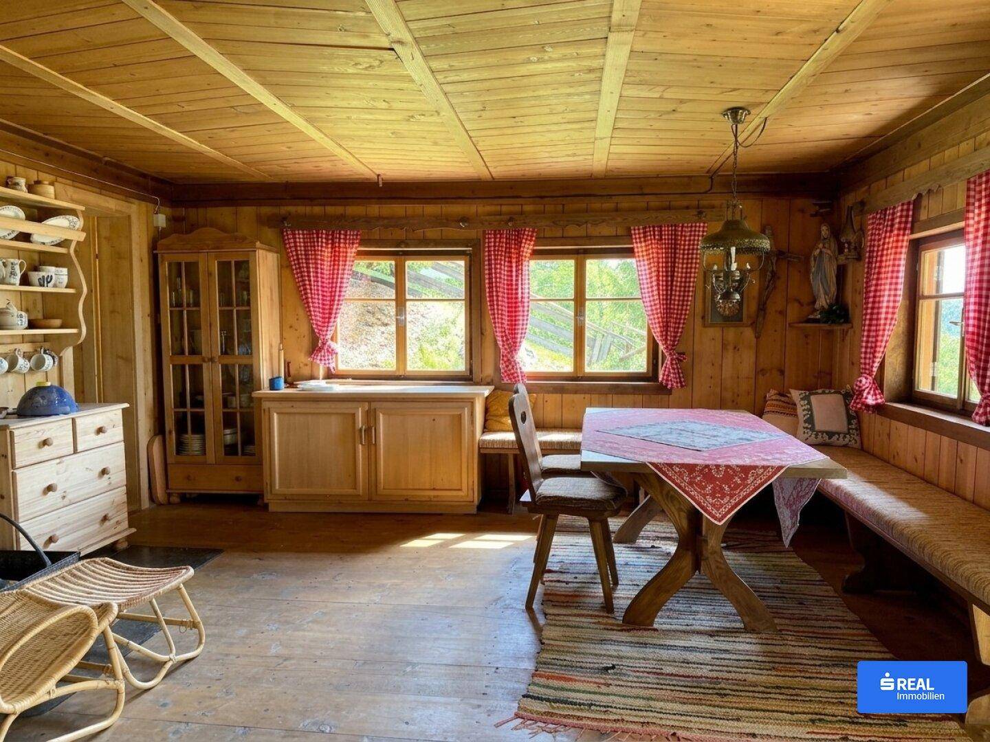 Gemütlicher Wohn-Essbereich im alpinen Stil mit Holztäfelung, rustikalen Möbeln und karierten Vorhängen.