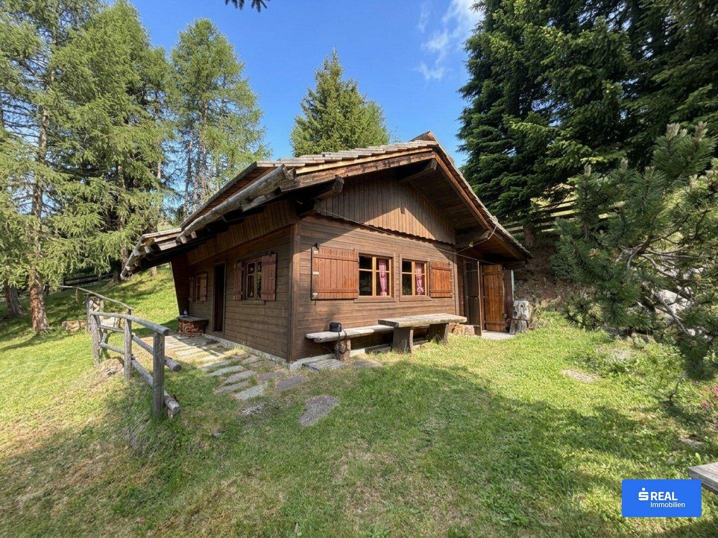 Rustikales Holzchalet mit traditionellen Fensterläden und einer kleinen Holzbank, umgeben von grünen Wiesen.