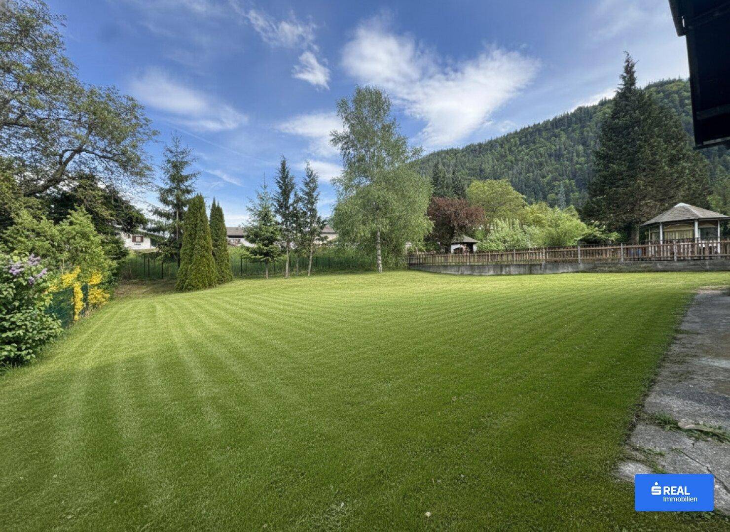 Großer, gepflegter Rasenbereich mit Streifenmuster und umgebenden Bäumen sowie Bergblick.