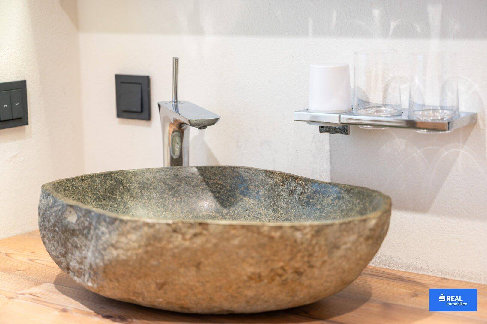 Modernes Badezimmer mit einem einzigartigen Waschbecken aus Naturstein auf einer Holzplatte.
