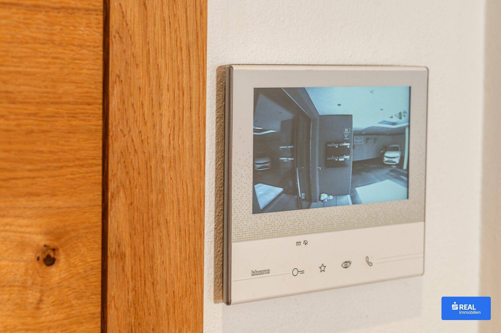 Modernes Gegensprechanlagensystem mit Bildschirm neben einer Holztür im Eingangsbereich.