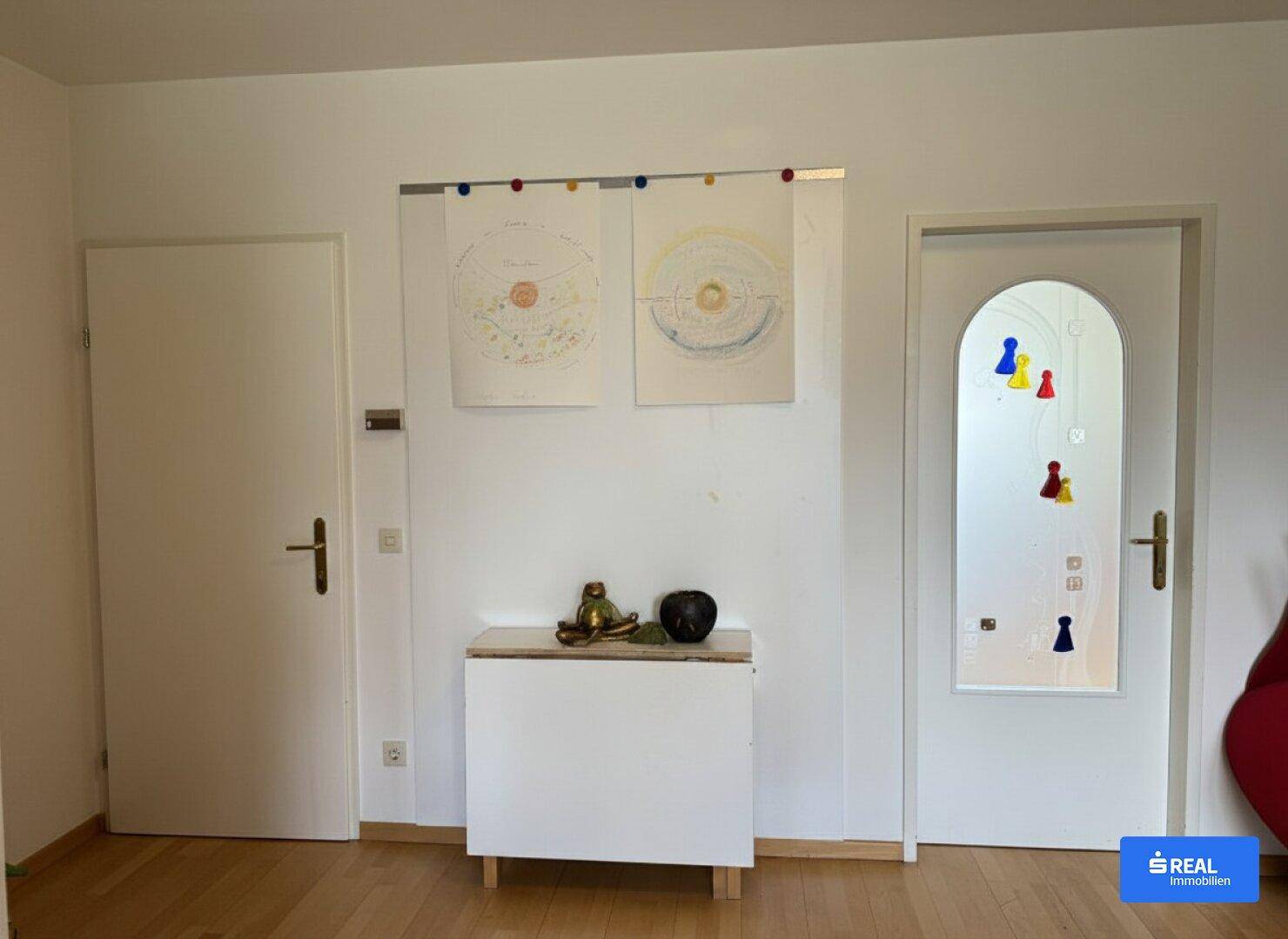 Heller Flur mit zwei weißen Türen, einem kleinen Schrank und Holzboden.