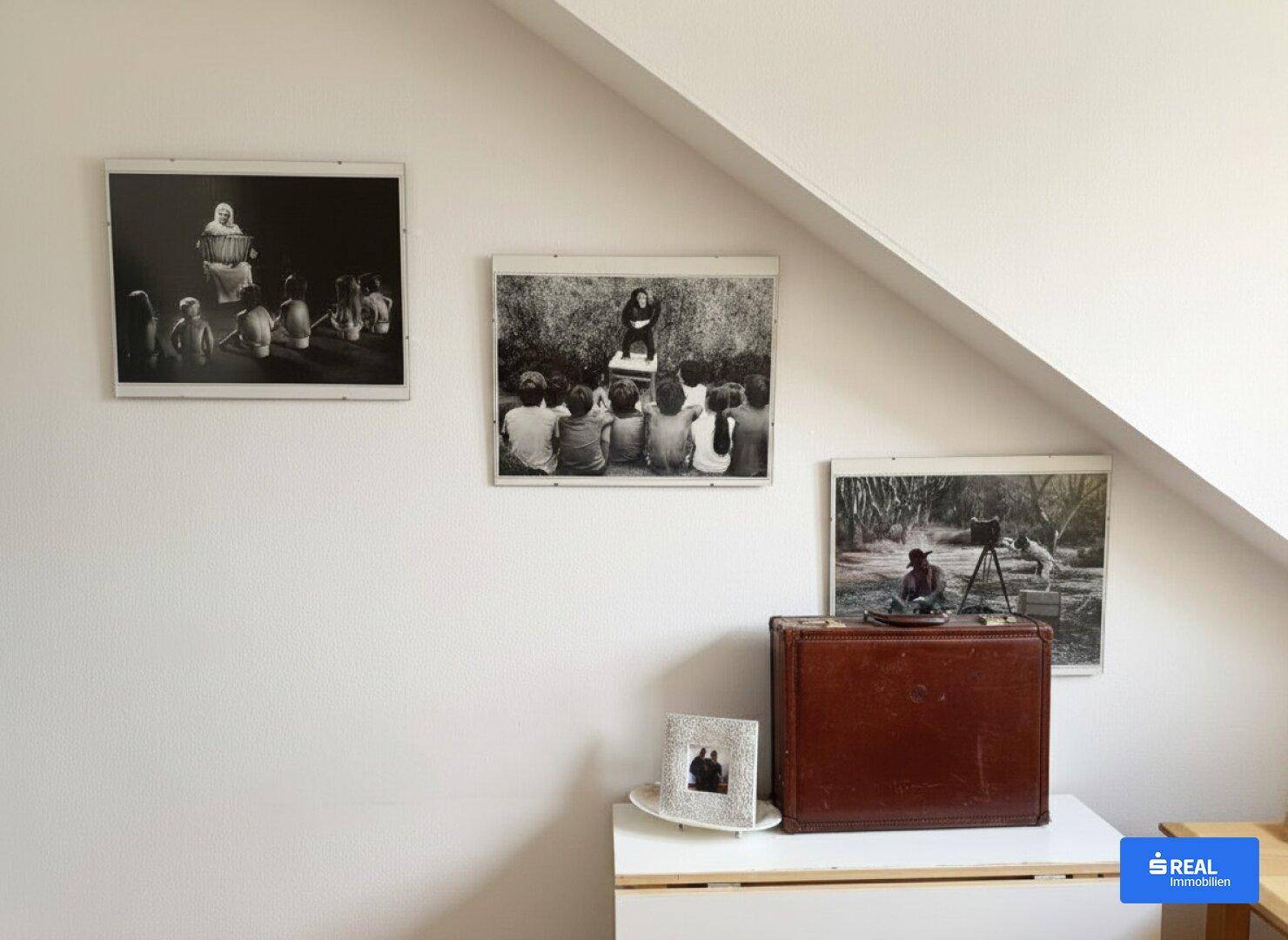Weiße Wand mit gerahmten Schwarz-Weiß-Bildern und einer Dachschräge in einem Wohnbereich.