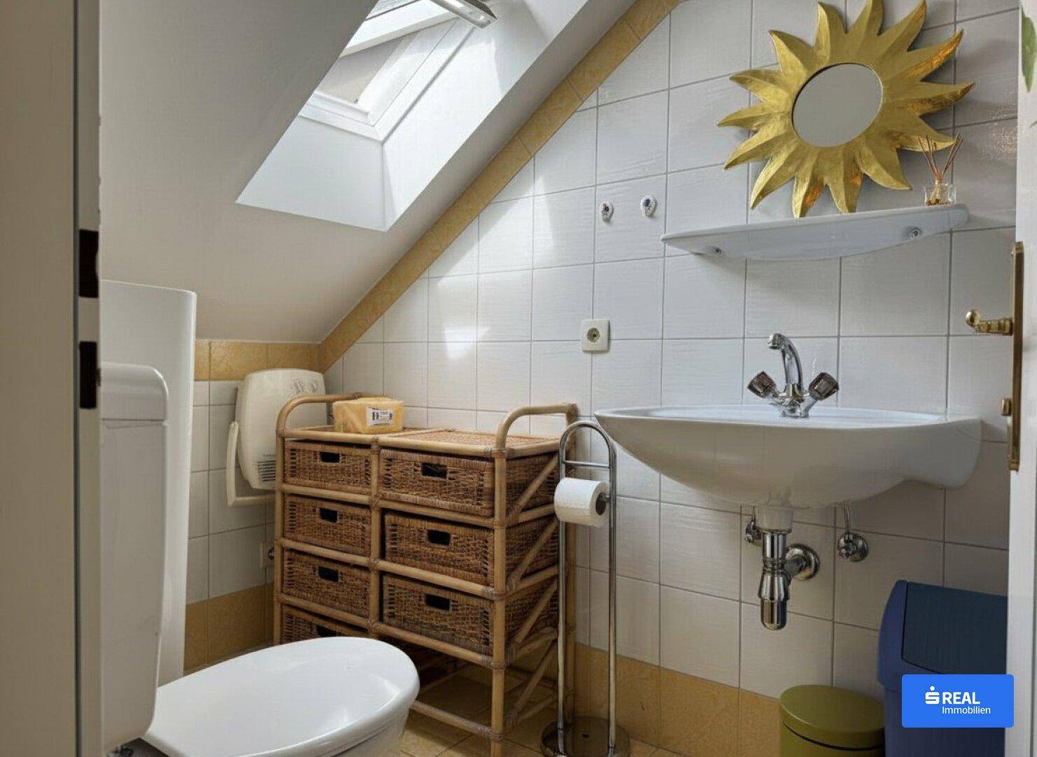 Badezimmer mit Dachschräge, WC, Waschbecken und einem Dachfenster für natürliches Licht.