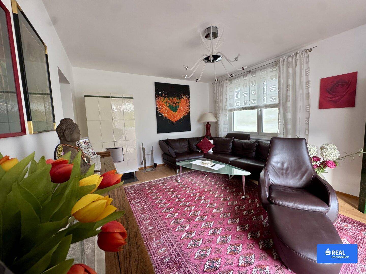 Wohnzimmer mit dunklem Ledersofa, Kachelofen und farbenfroher Dekoration.