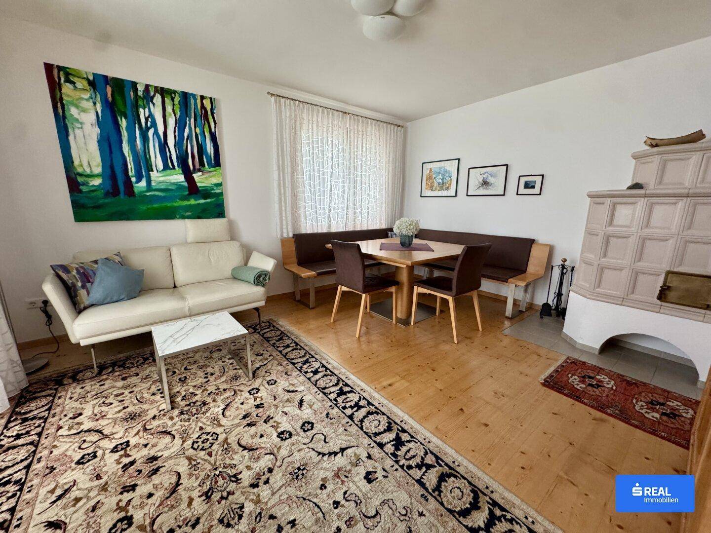 Offener Wohn- und Essbereich mit Kachelofen und hellem Sofa.