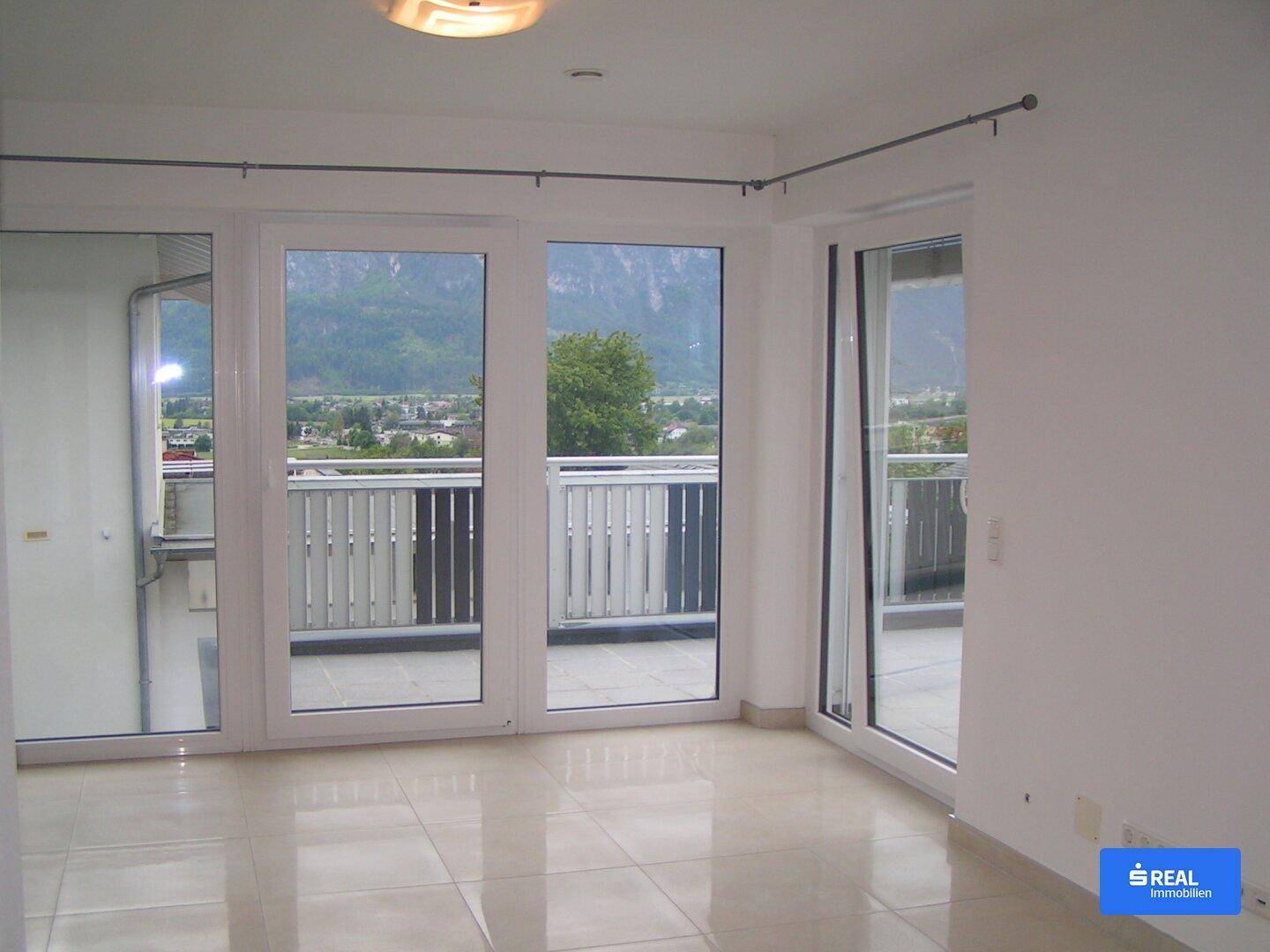 Heller Wohnraum mit großen Fenstern, direktem Zugang zur Terrasse und weitem Bergblick.