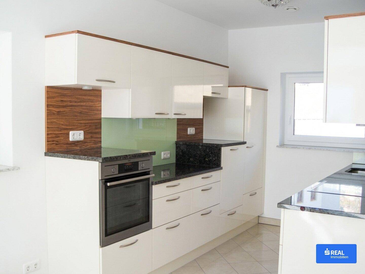Moderne Einbauküche mit weißen Hochglanzfronten, dunklen Granitarbeitsplatten und integriertem Backofen.