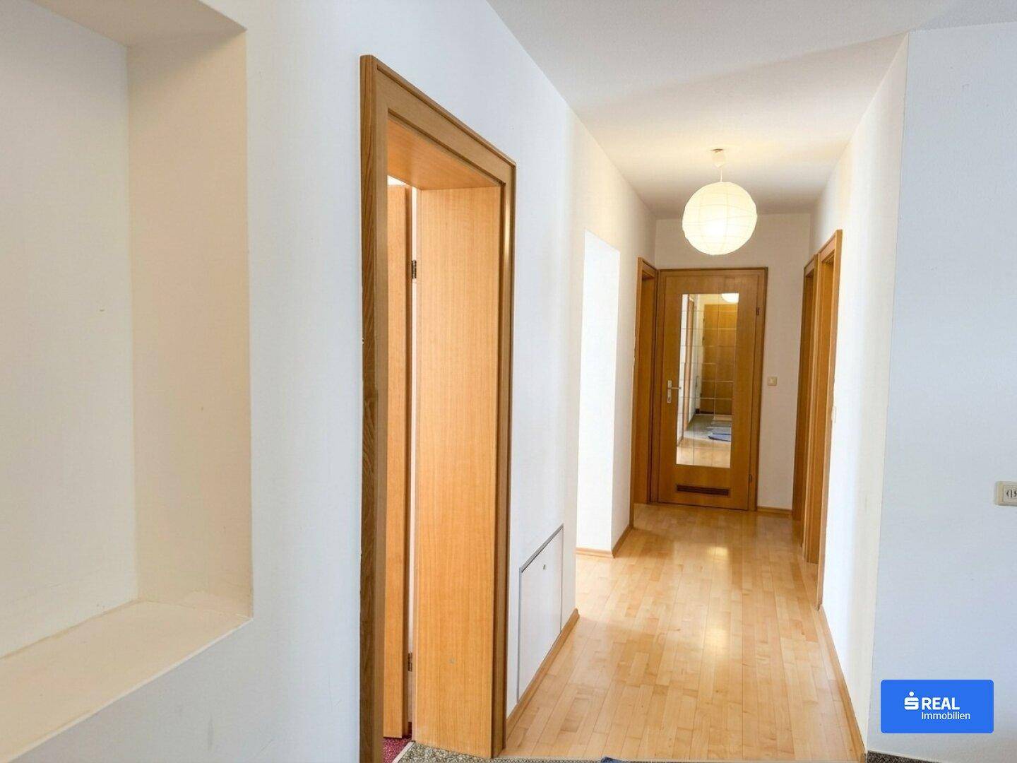 Heller Flur mit Holzparkettboden und Holztüren, der zu verschiedenen Räumen führt.