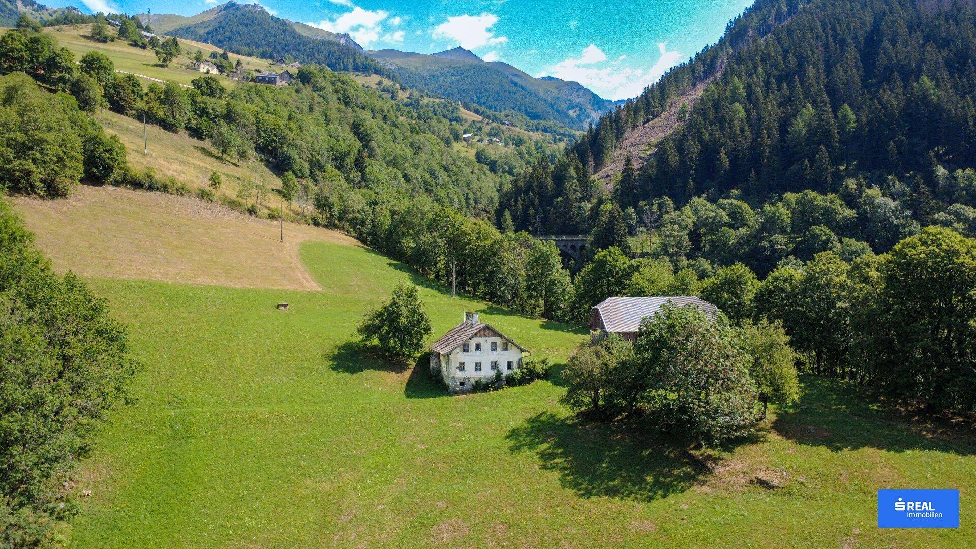 Weitläufiger Blick auf die ländliche Umgebung mit zwei Gebäuden in einem grünen Tal.