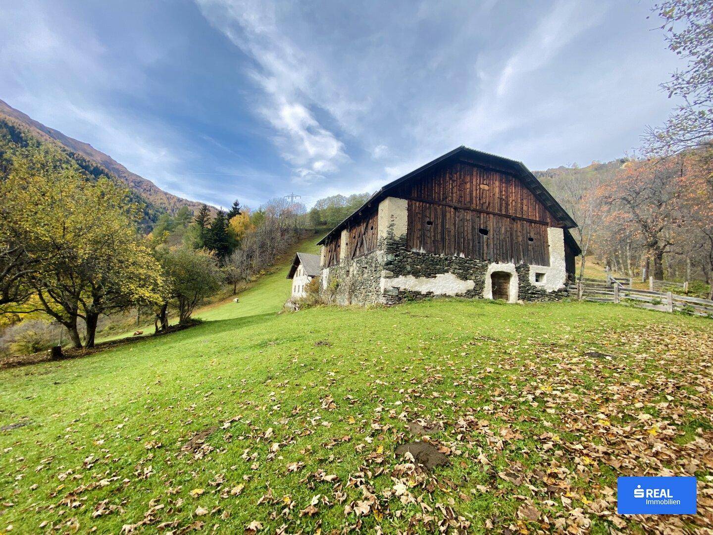 Altes Bauernhaus mit Holzwänden und Steinfundament in herbstlicher Berglandschaft.