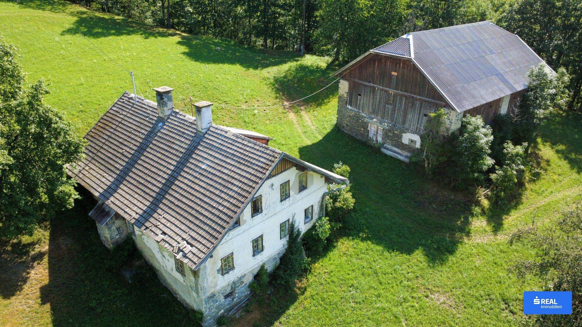 Draufsicht auf zwei traditionelle Gebäude, umgeben von grünen Wiesen und Bäumen.