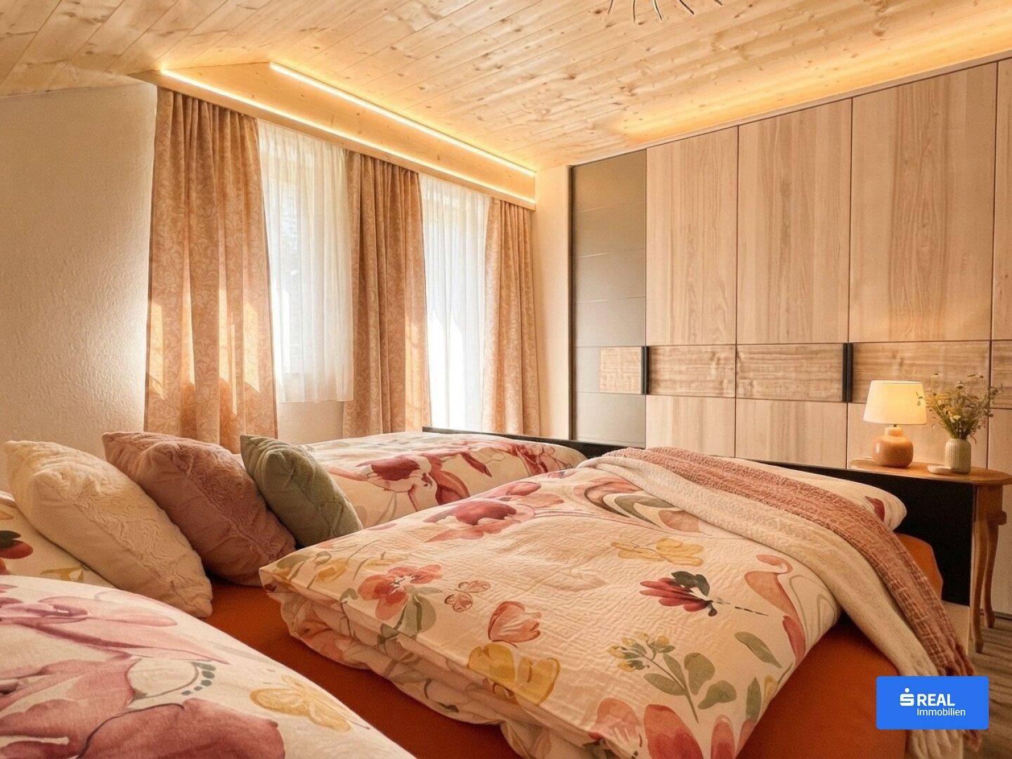 Gemütliches Schlafzimmer mit Holzdecke, floralen Bettdecken und integrierten Schränken.
