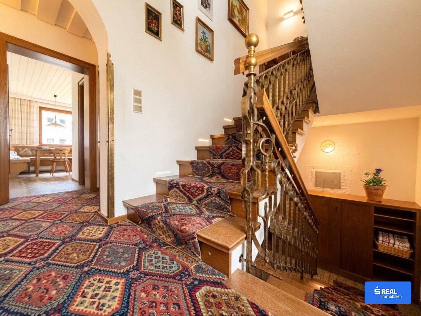 Treppenhaus mit kunstvollem Geländer, gemustertem Teppich und Zugang zu weiteren Räumen.