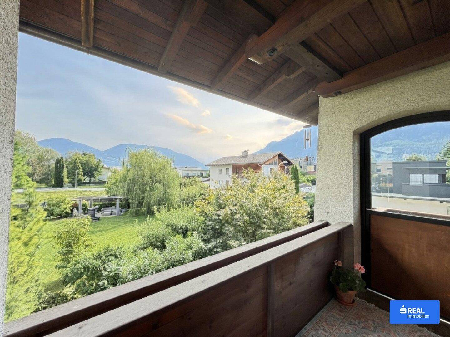 Balkon mit Holzboden und Geländer bietet einen weiten Blick auf die grüne Landschaft und Berge.