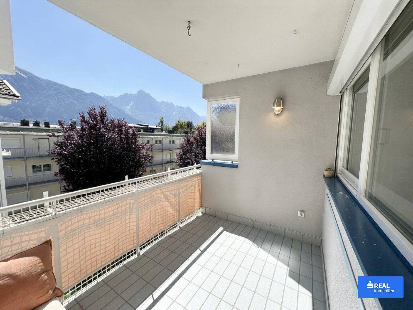 Sonniger Balkon mit Fliesenboden, Markise und einem weiten Blick auf die umliegende Berglandschaft.