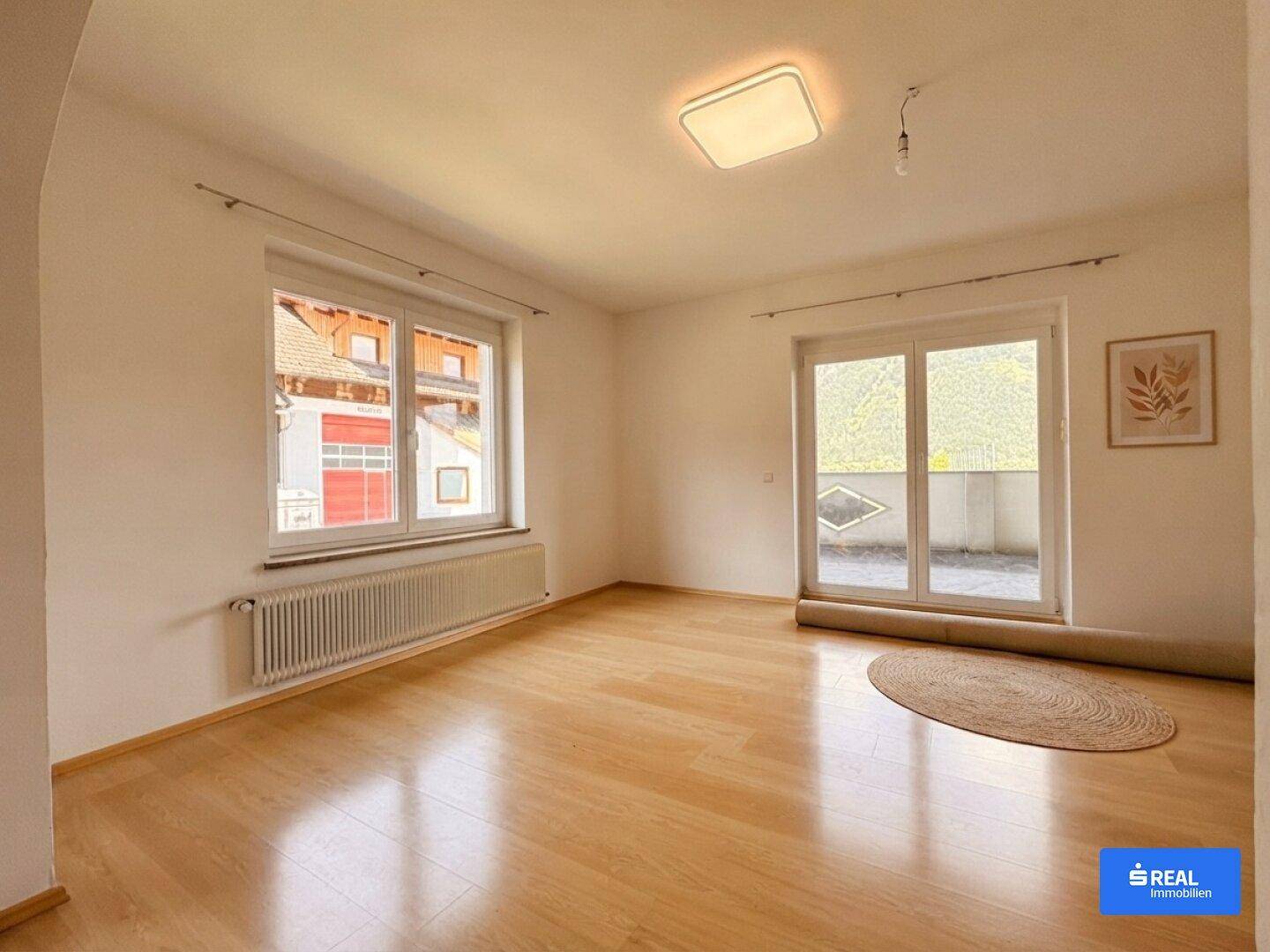 Geräumiger Raum mit Holzboden, großem Fenster und Zugang zu einem Balkon mit Bergblick.