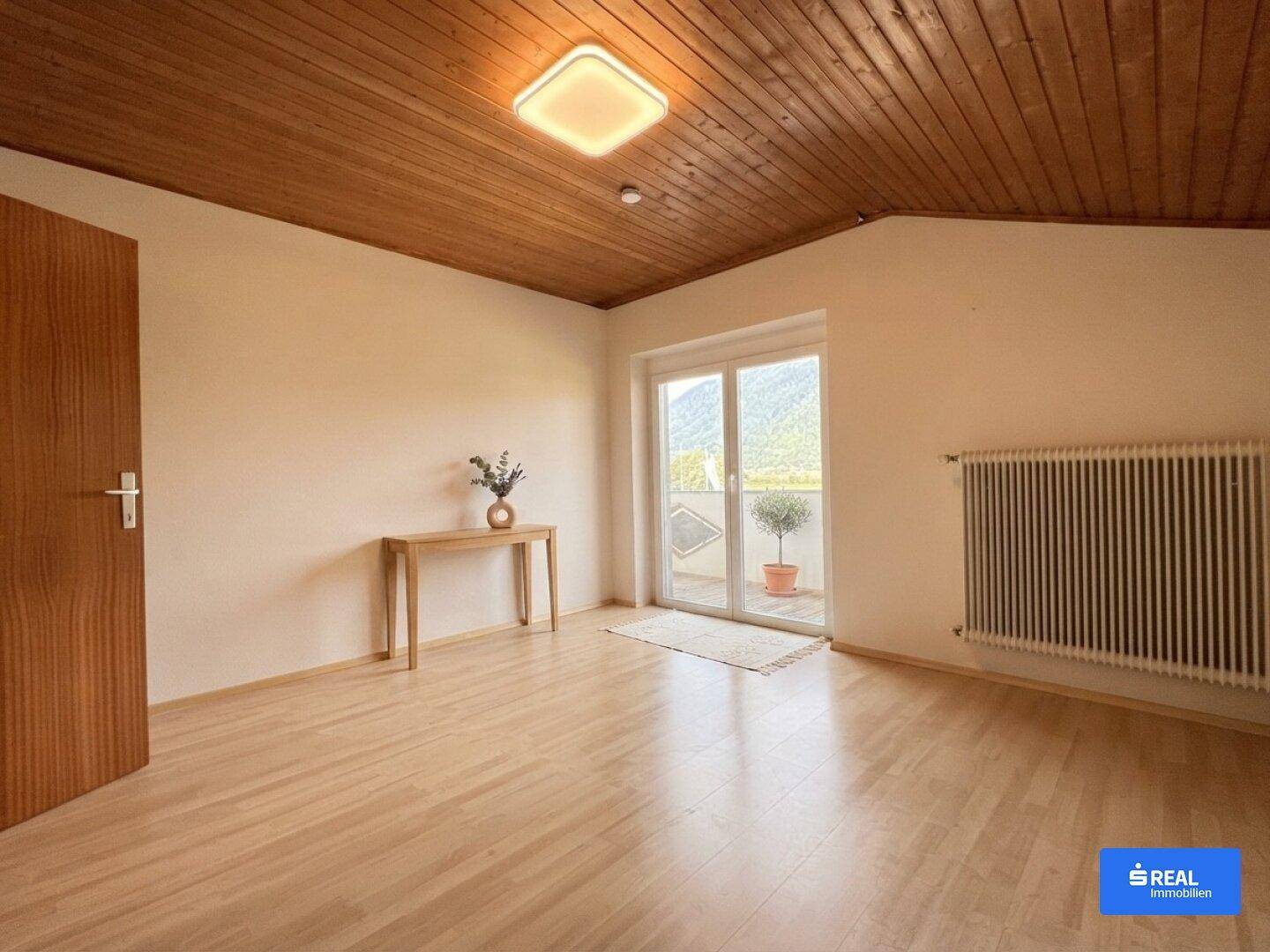 Helles Schlafzimmer im Dachgeschoss mit Holzboden, Holzdecke und Balkonzugang.