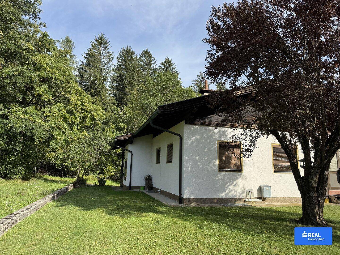 Seitenansicht des Hauses mit weitläufiger Rasenfläche und altem Baumbestand in ländlicher Umgebung.