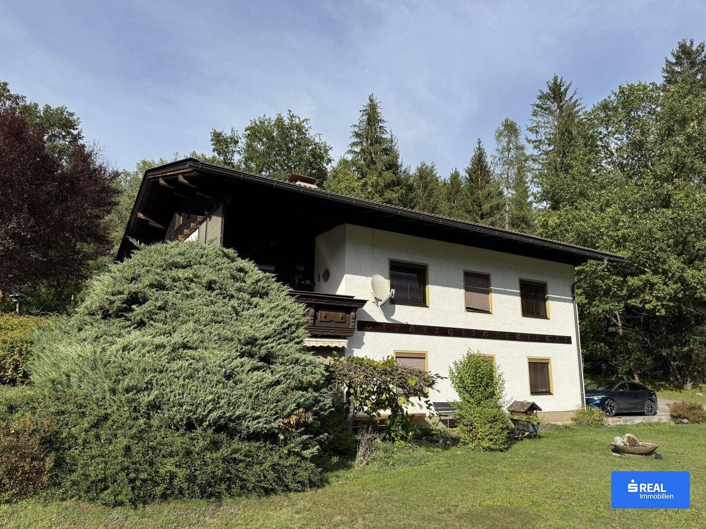Traditionelles Landhaus mit weißer Fassade, Holzbalkonen und einem gepflegten Gartenbereich.