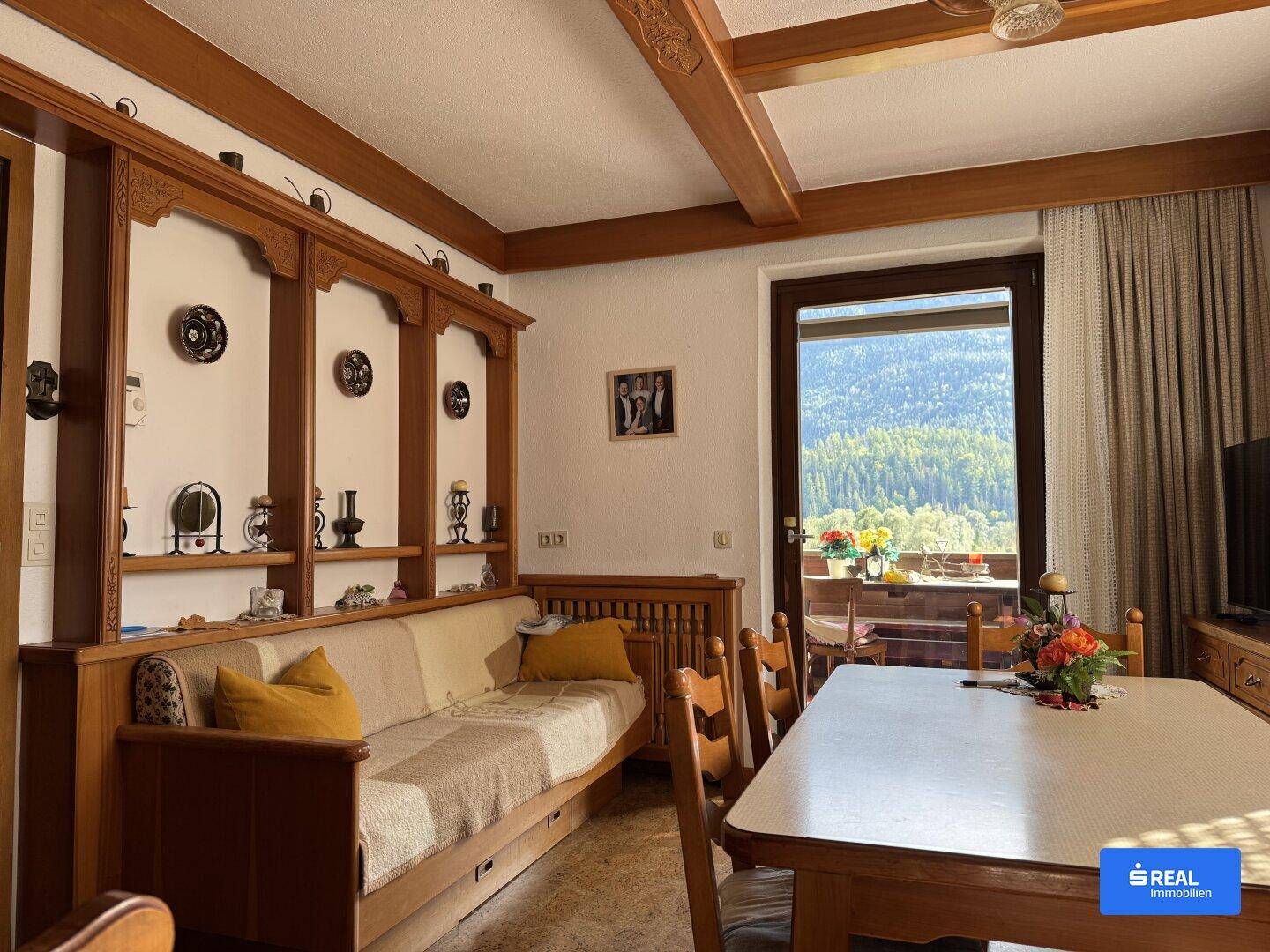 Gemütlicher Wohn- und Essbereich im alpinen Stil mit Holzbalken und Bergblick vom Balkon.