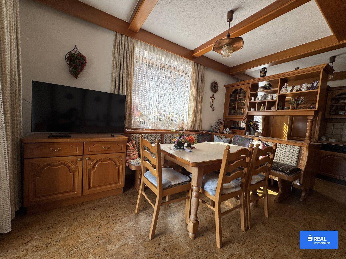 Traditioneller Essbereich mit Holztisch, Stühlen und einem großen Schrank, hell durch ein Fenster.