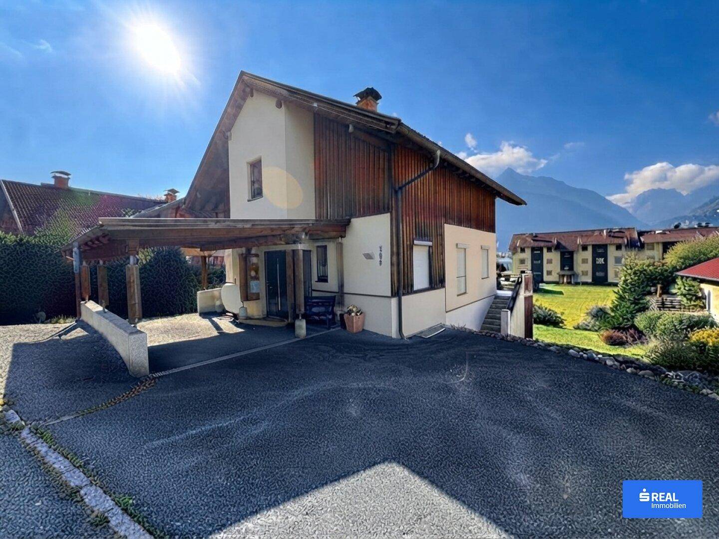 Vorderansicht des Hauses mit Carport, Auffahrt und Bergblick im Hintergrund.