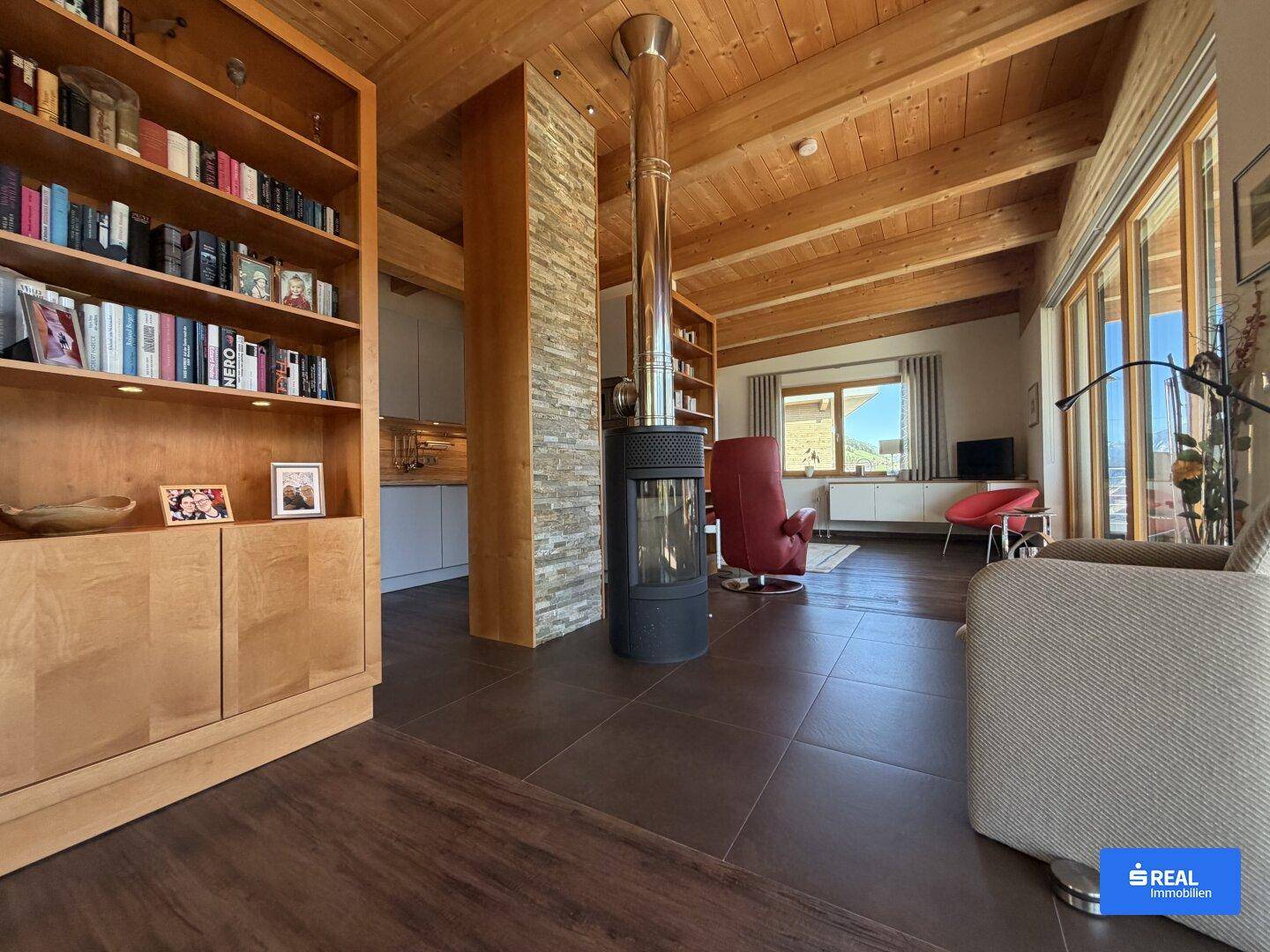 Gemütliches Wohnzimmer mit modernem Kaminofen, Holzbalkendecke und großem Bücherregal.