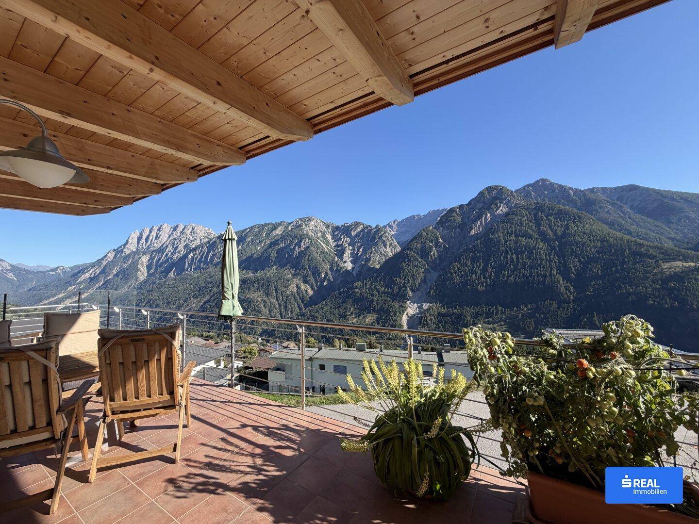 Weitläufige Terrasse mit Holzmöbeln und einem beeindruckenden Panoramablick auf die umliegenden Berge.