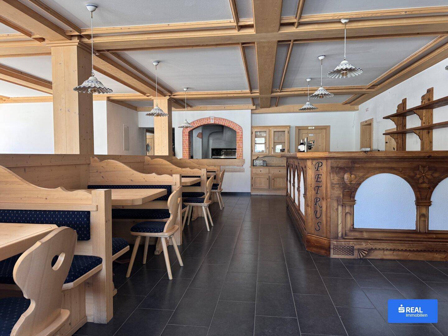 Innenansicht des Restaurants mit Holzbänken, einer Bar und einem traditionellen Pizzaofen im Hintergrund.