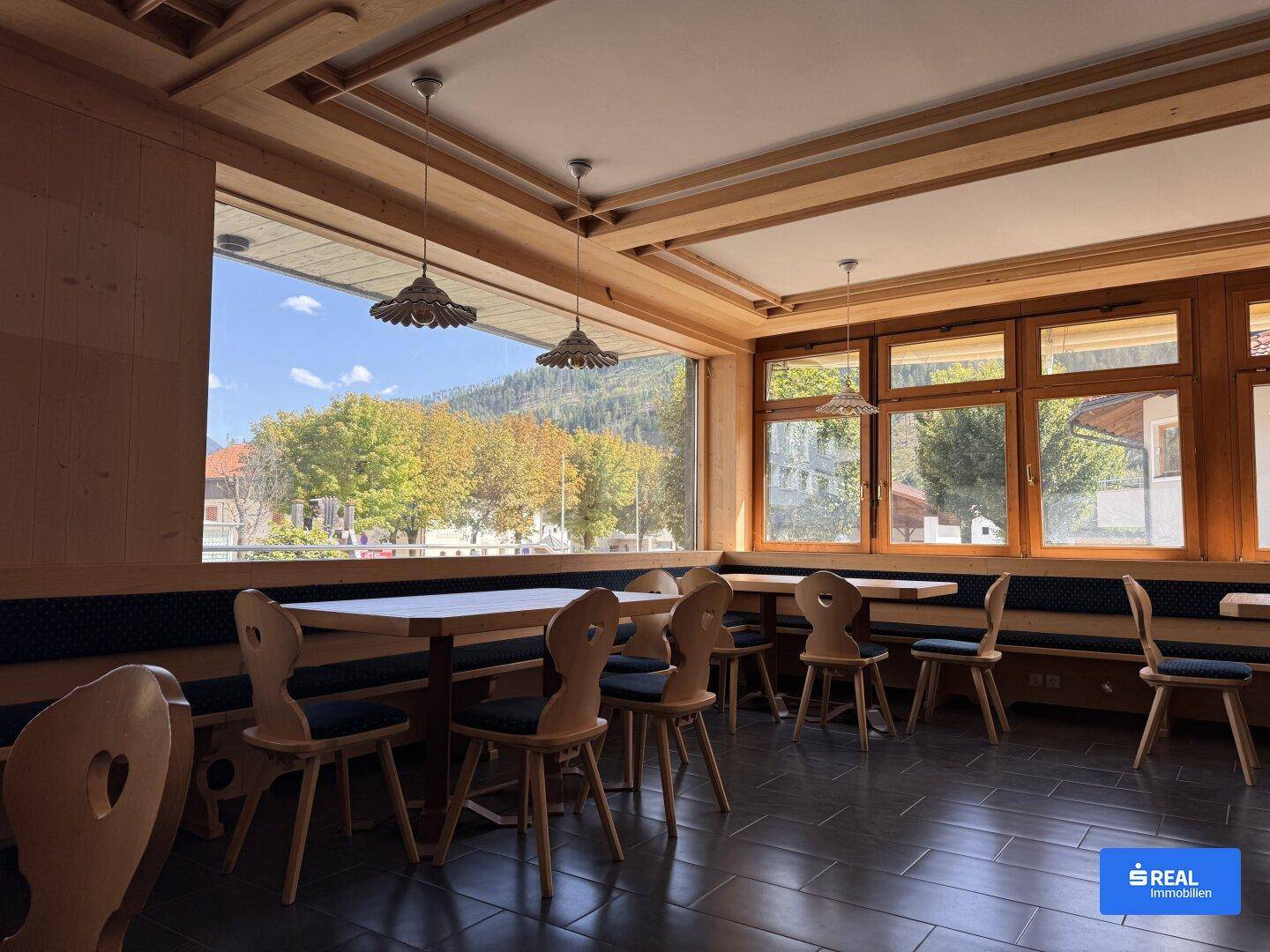 Gemütlicher Essbereich mit Holztischen und Bänken, großen Fenstern und einem weiten Blick auf die umliegende Landschaft.