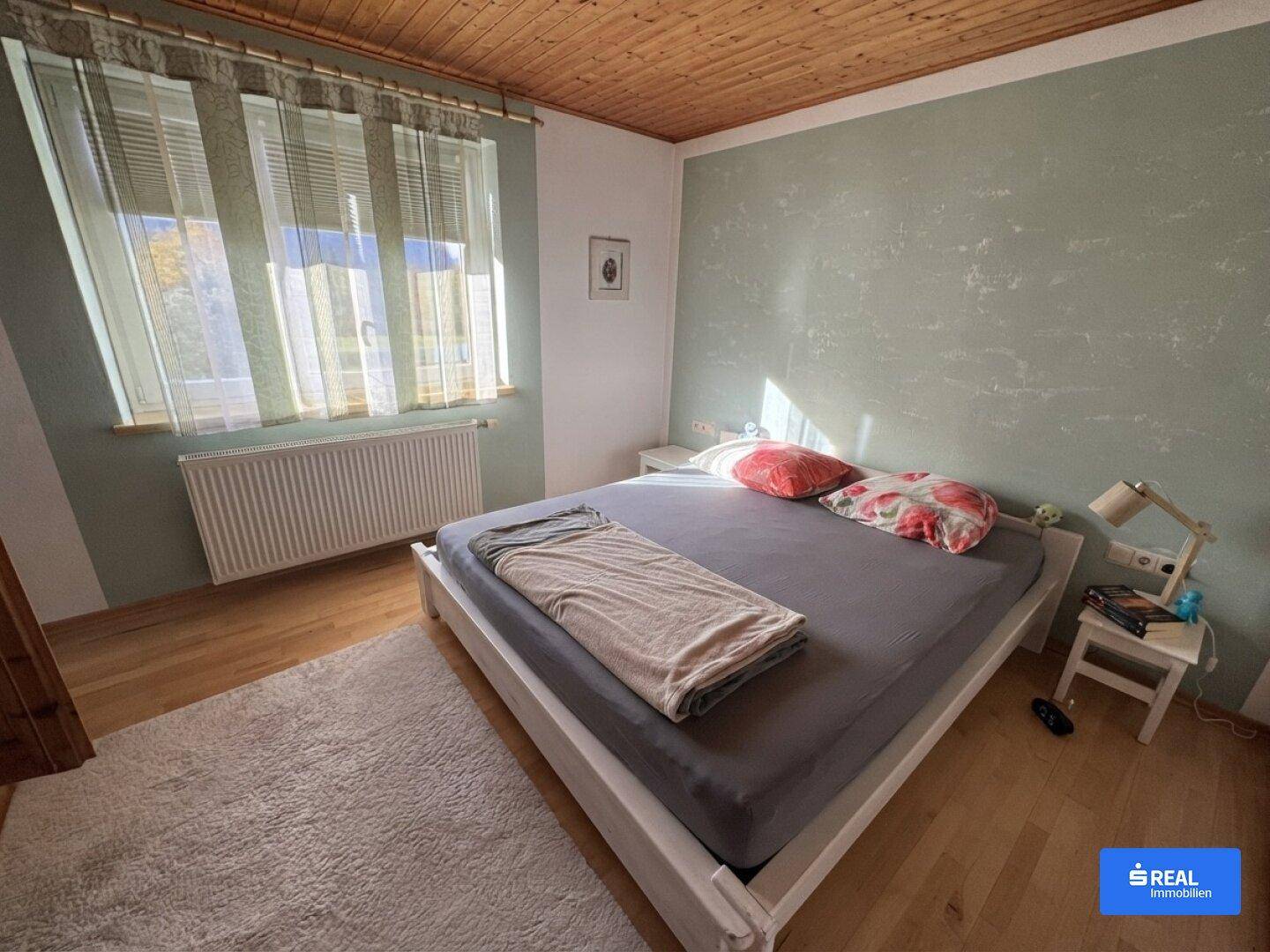 Helles Schlafzimmer mit Holzboden, grüner Akzentwand und großem Fenster.