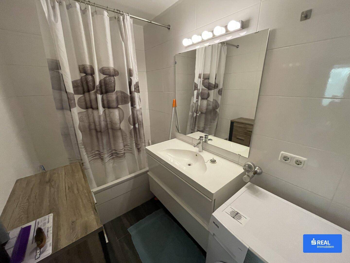 Modernes Badezimmer mit Dusche, Waschbecken, großem Spiegel und integrierter Waschmaschine.
