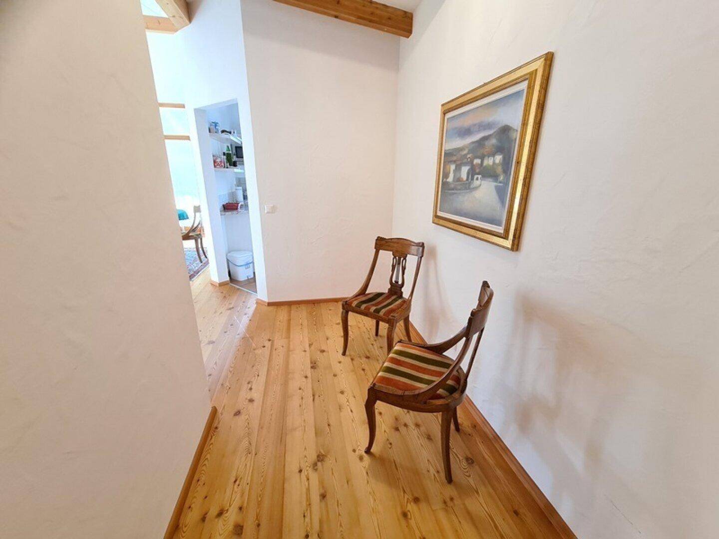 Langer Flur mit Holzboden und einem Gemälde, der einen Blick in einen angrenzenden Raum bietet.