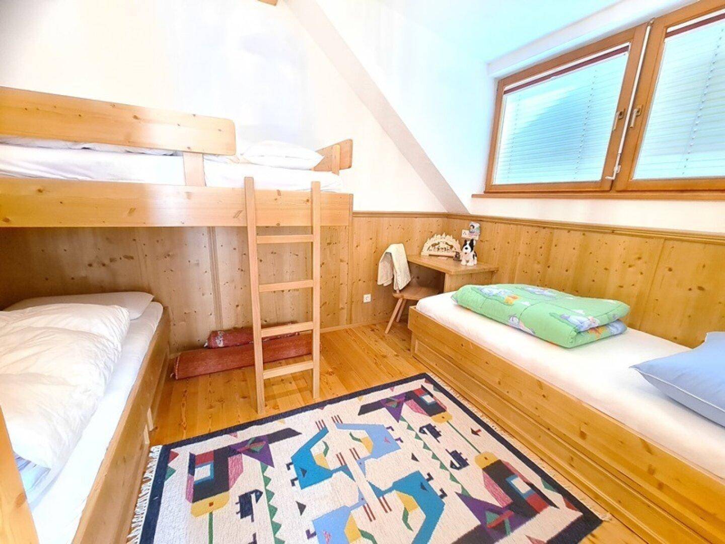 Gemütliches Schlafzimmer mit Holzwänden, Etagenbett und einem Einzelbett unter einer Dachschräge.