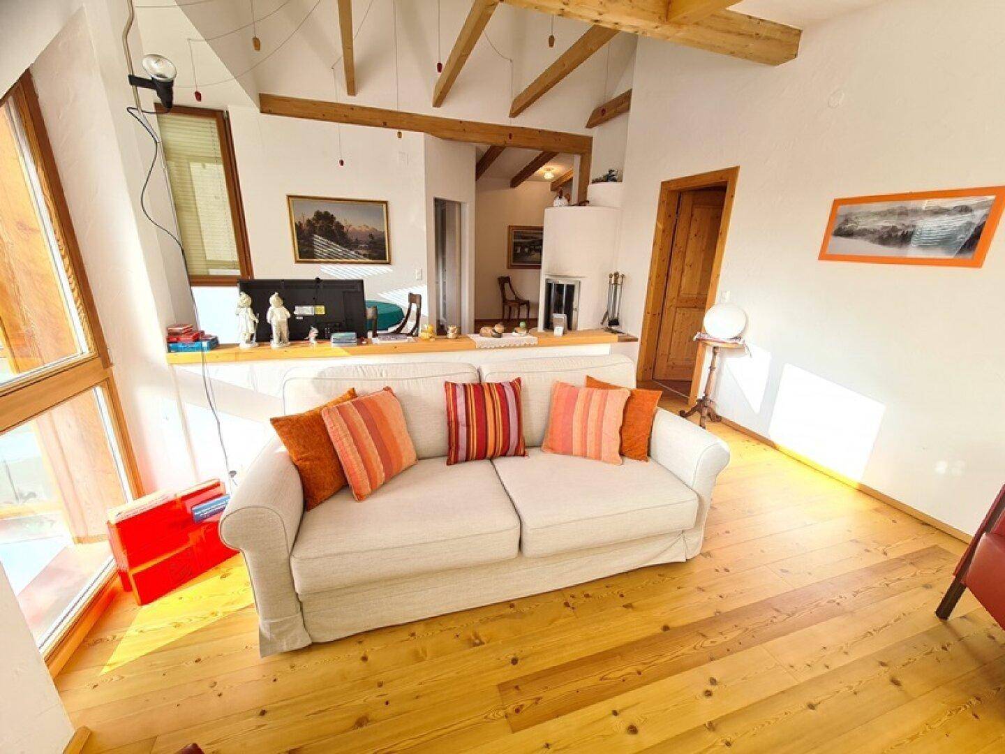 Helles Wohnzimmer mit Holzbalken, Holzboden und einem gemütlichen Sofa, das viel Tageslicht erhält.
