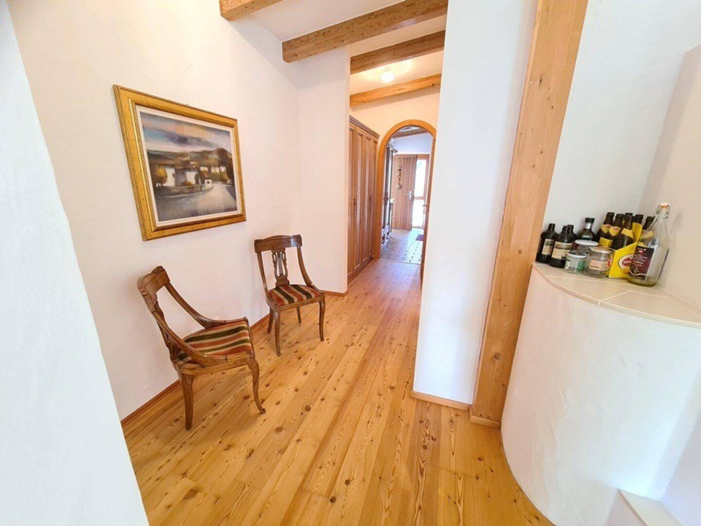 Heller Flur mit Holzboden, Holzbalken und einem Gemälde an der Wand, der zu weiteren Räumen führt.