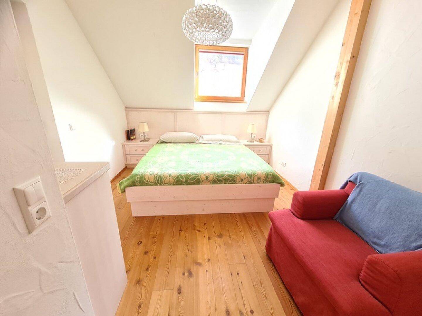 Gemütliches Schlafzimmer im Dachgeschoss mit Holzboden, Dachfenster und schrägen Wänden.