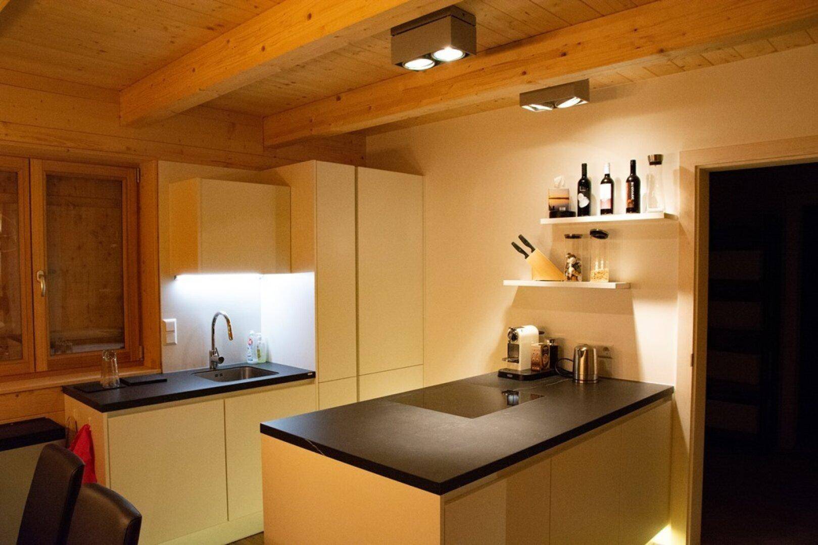 Helle Küche mit weißen Schränken, dunkler Arbeitsplatte und Holzbalkendecke.