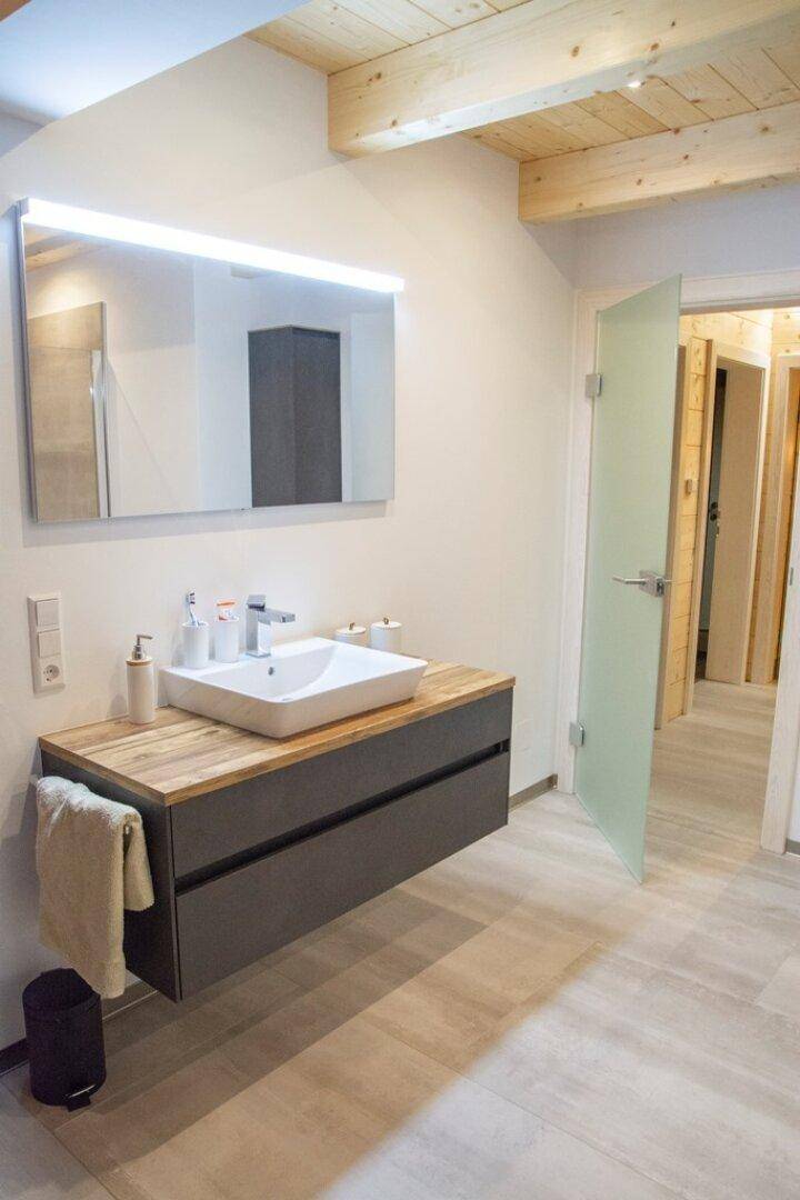 Modernes Badezimmer mit schwebendem Waschtisch, Holzplatte und großem Spiegel.