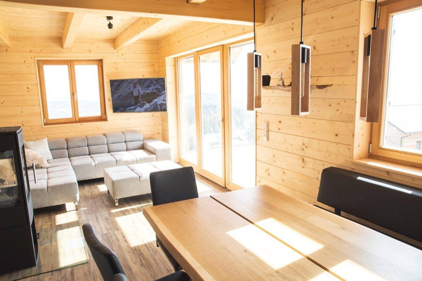 Heller Wohn-Essbereich mit großen Fenstern, Holzwänden und Bergblick.