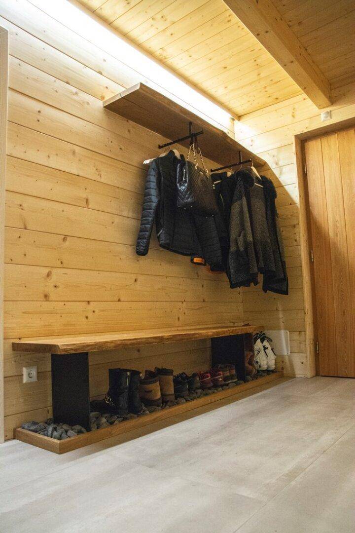Eingangsbereich mit Holzwänden, offener Garderobe und Ablage für Schuhe.