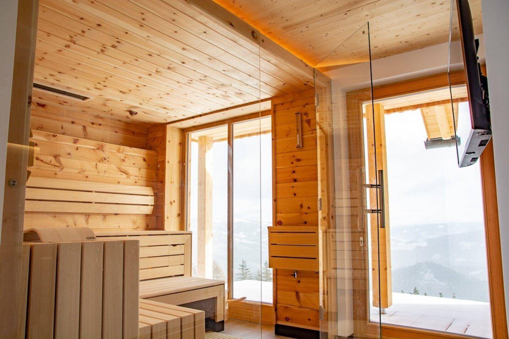 Geräumige Sauna mit Holzbänken, großen Fenstern und Panoramablick auf die Berge.