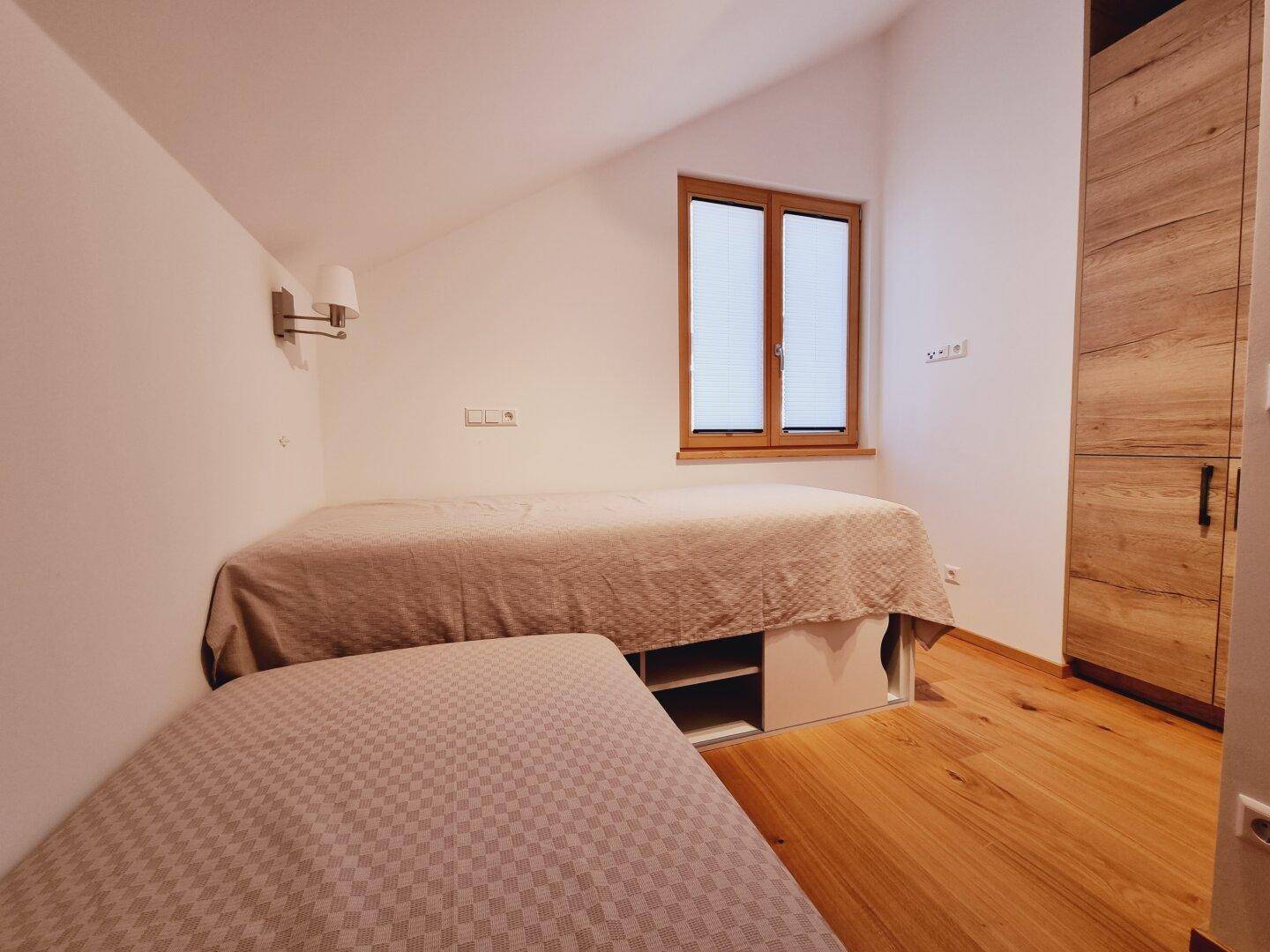 Helles Schlafzimmer mit zwei Einzelbetten, Holzschrank und Fenster im Dachgeschoss.