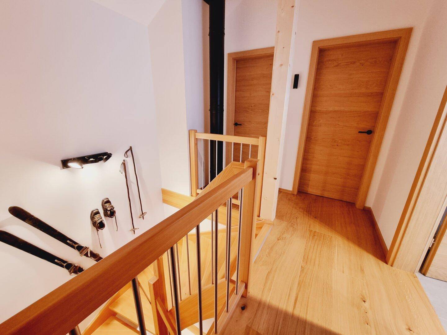Oberer Treppenabsatz mit Holztüren zu den Zimmern und dekorativen Skiern an der Wand.