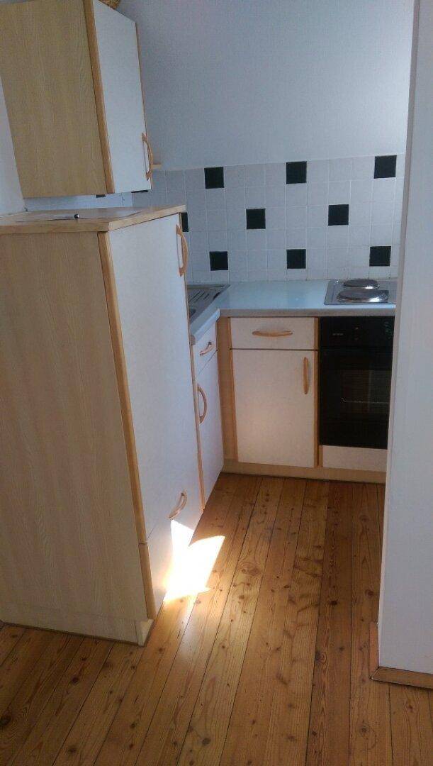 Kleine Einbauküche mit hellen Holzschränken, Kochfeld und Holzdielenboden.