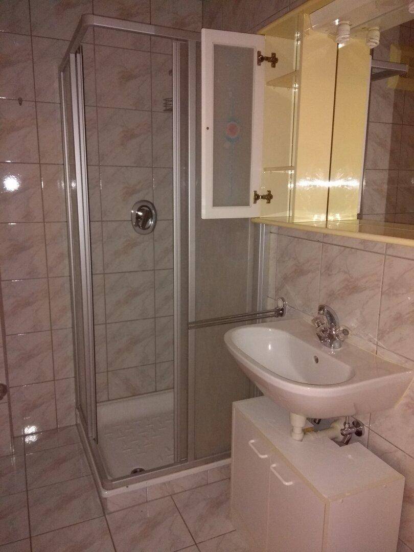 Badezimmer mit Duschkabine, Waschbecken und hellen Fliesen an Wänden und Boden.